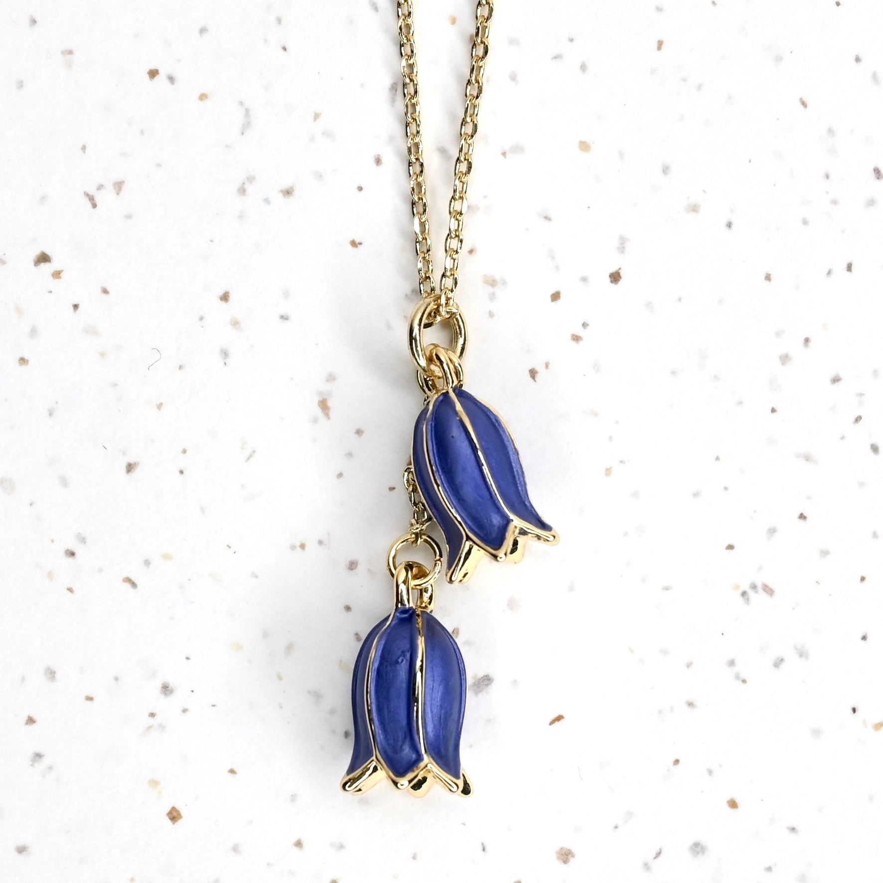 Closeup of 2 bluebells hanging from a gold necklace