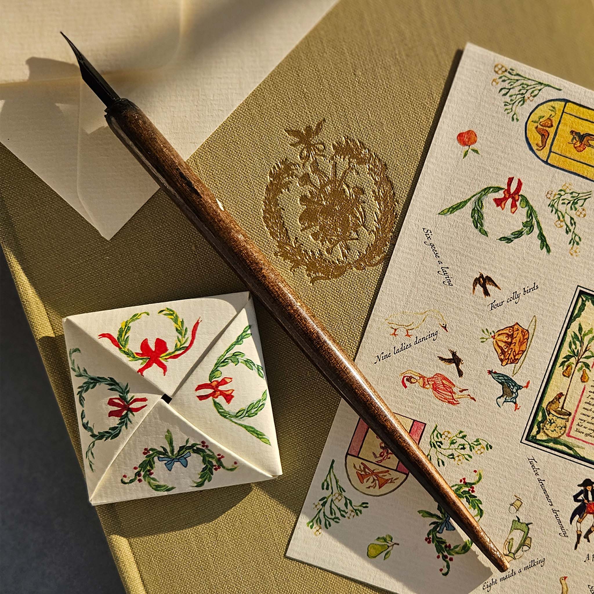 Decorative Christmas cards with floral designs and a quill pen on a textured surface.