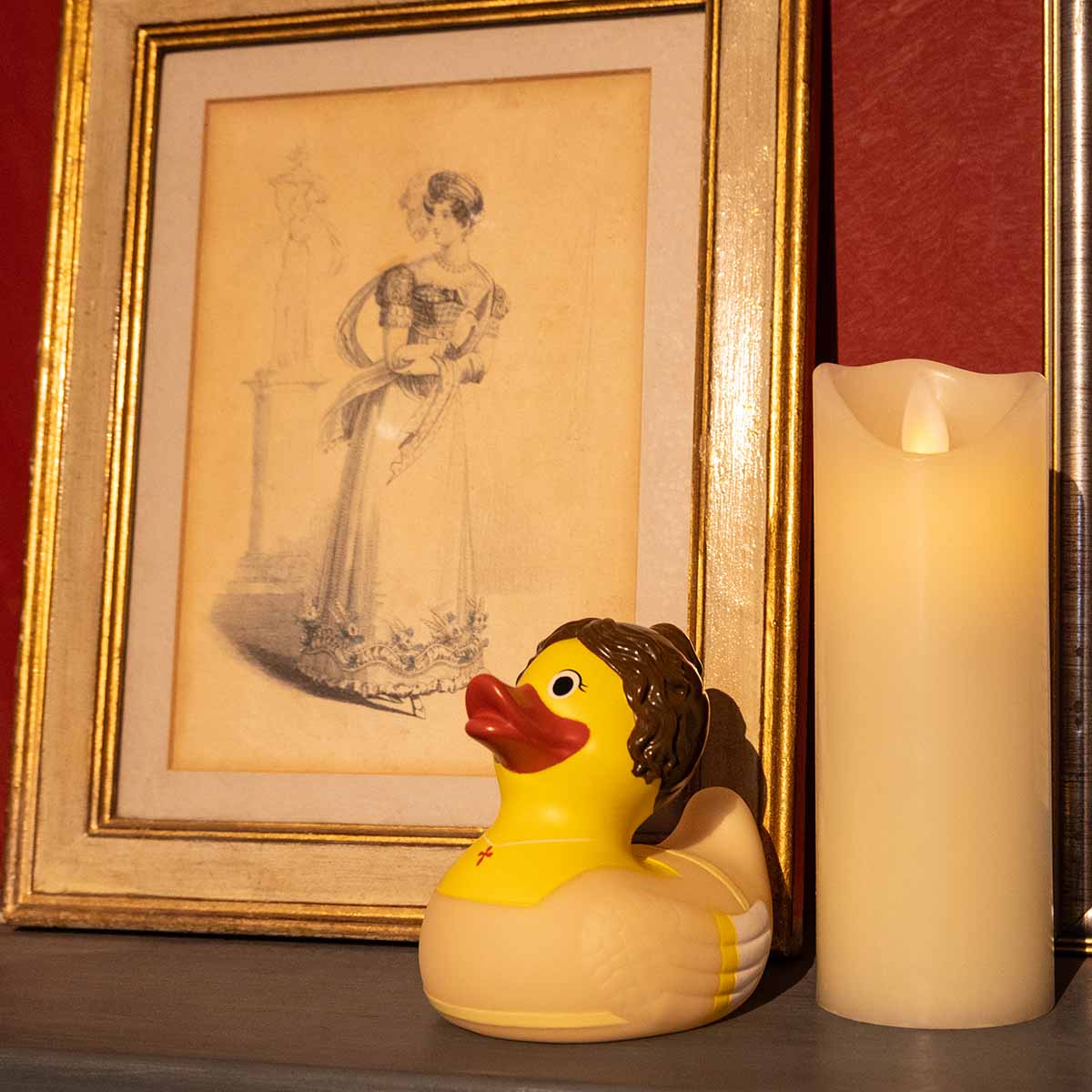 Elizabeth Bennet Rubber Duck positioned next to a Regency illustration in a frame and a lit candle.