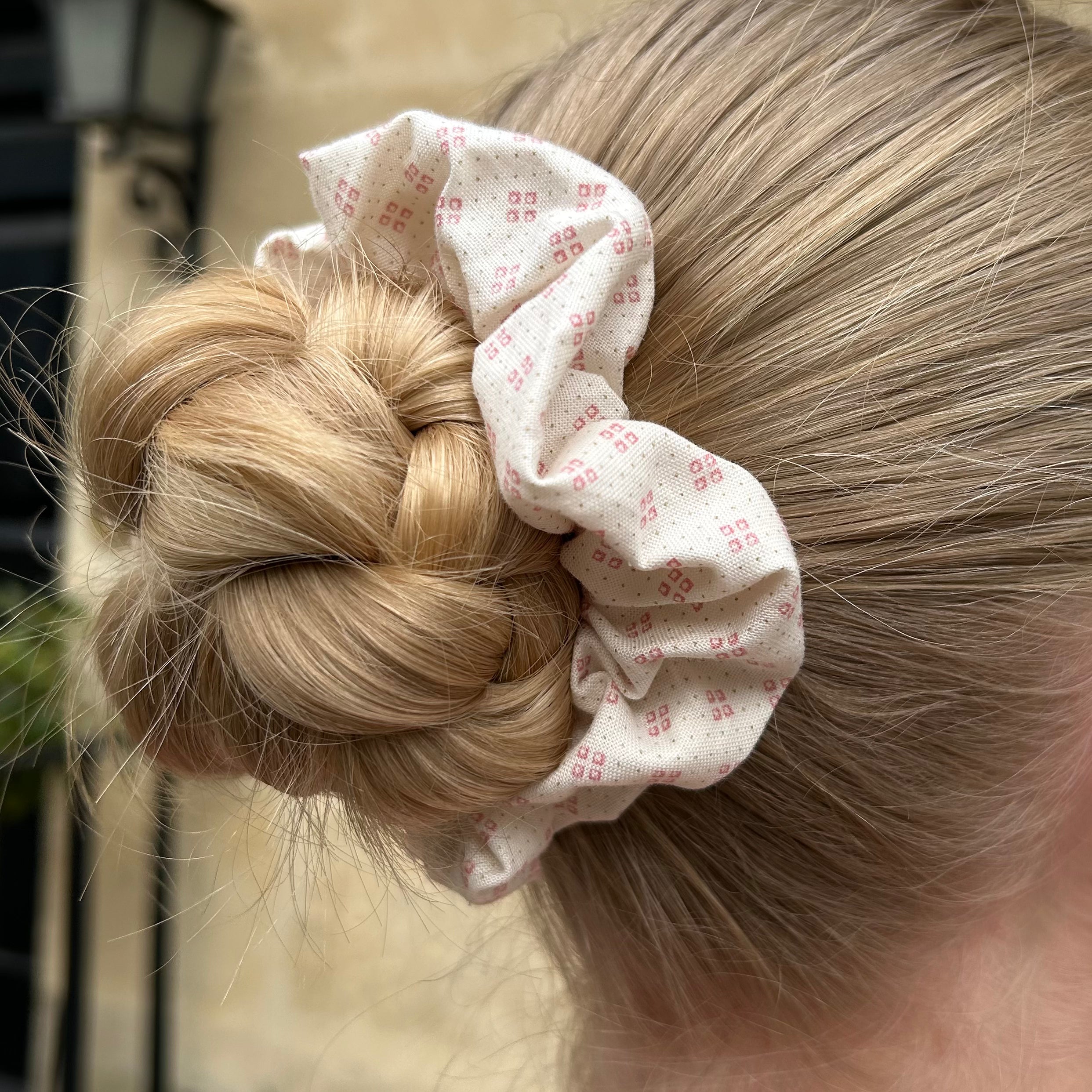 Pink patterned scrunchie shown on hair in a bun.