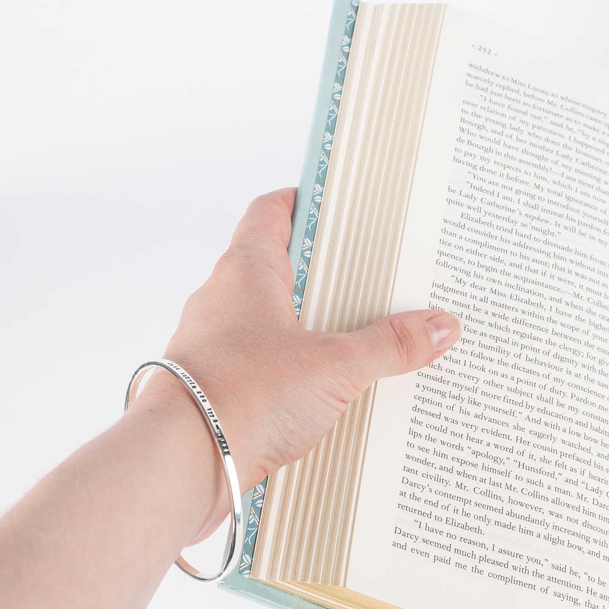 Silver bracelet shown on hand holding an open book.