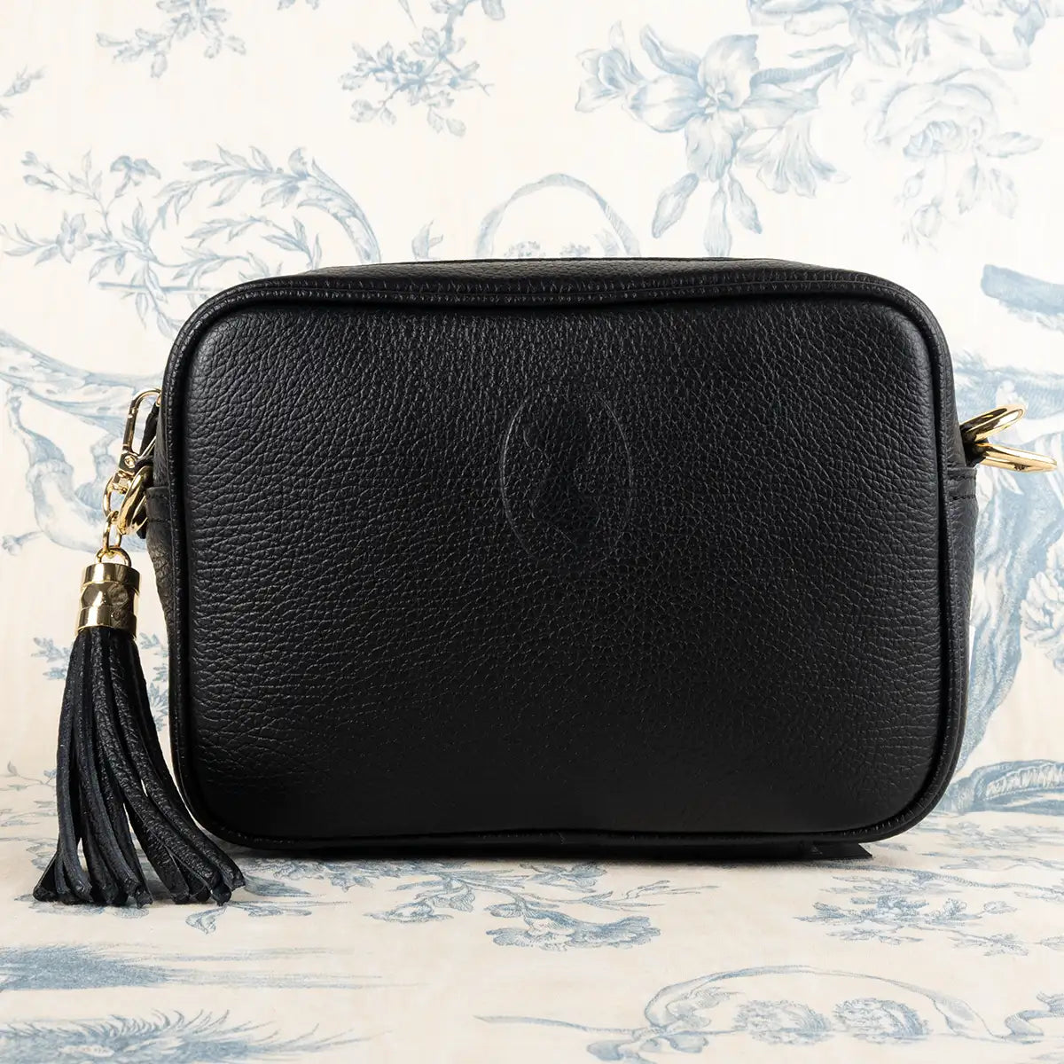 Black leather crossbody bag with a tassel on a decorative white and blue background
