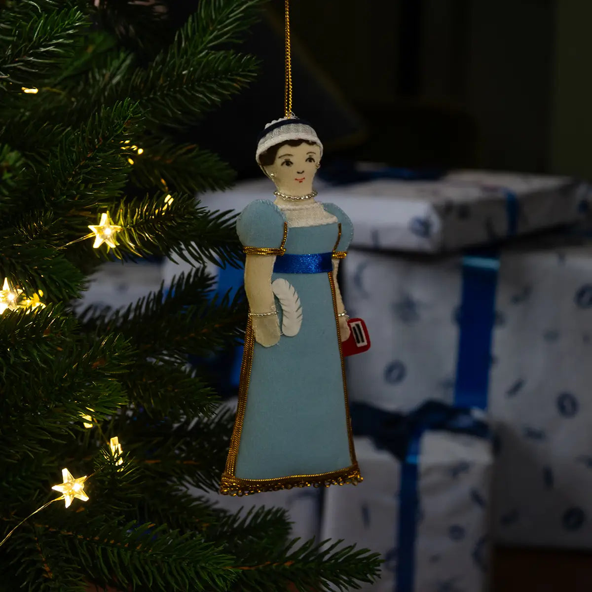 Christmas scene of the doll decoration hanging on a Christmas tree next to a glowing fire.