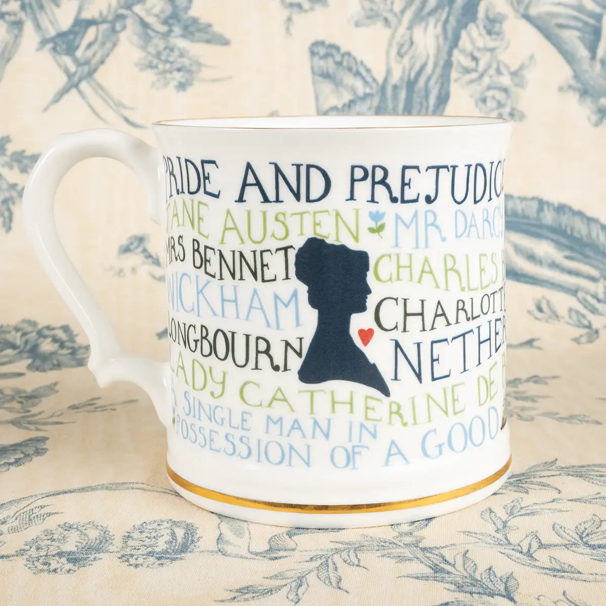 Tazza in edizione limitata con testo verde e blu di 'Pride and Prejudice' di Jane Austen su uno sfondo floreale con una silhouette e un cuore rosso al centro.
