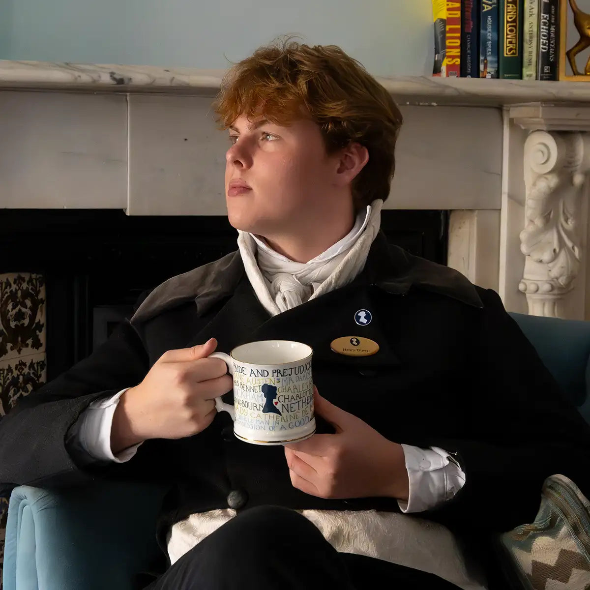 Man sitting in a cozy room at the Queensberry Hotel, Bath, holding a mug, with a fireplace and books in the background.