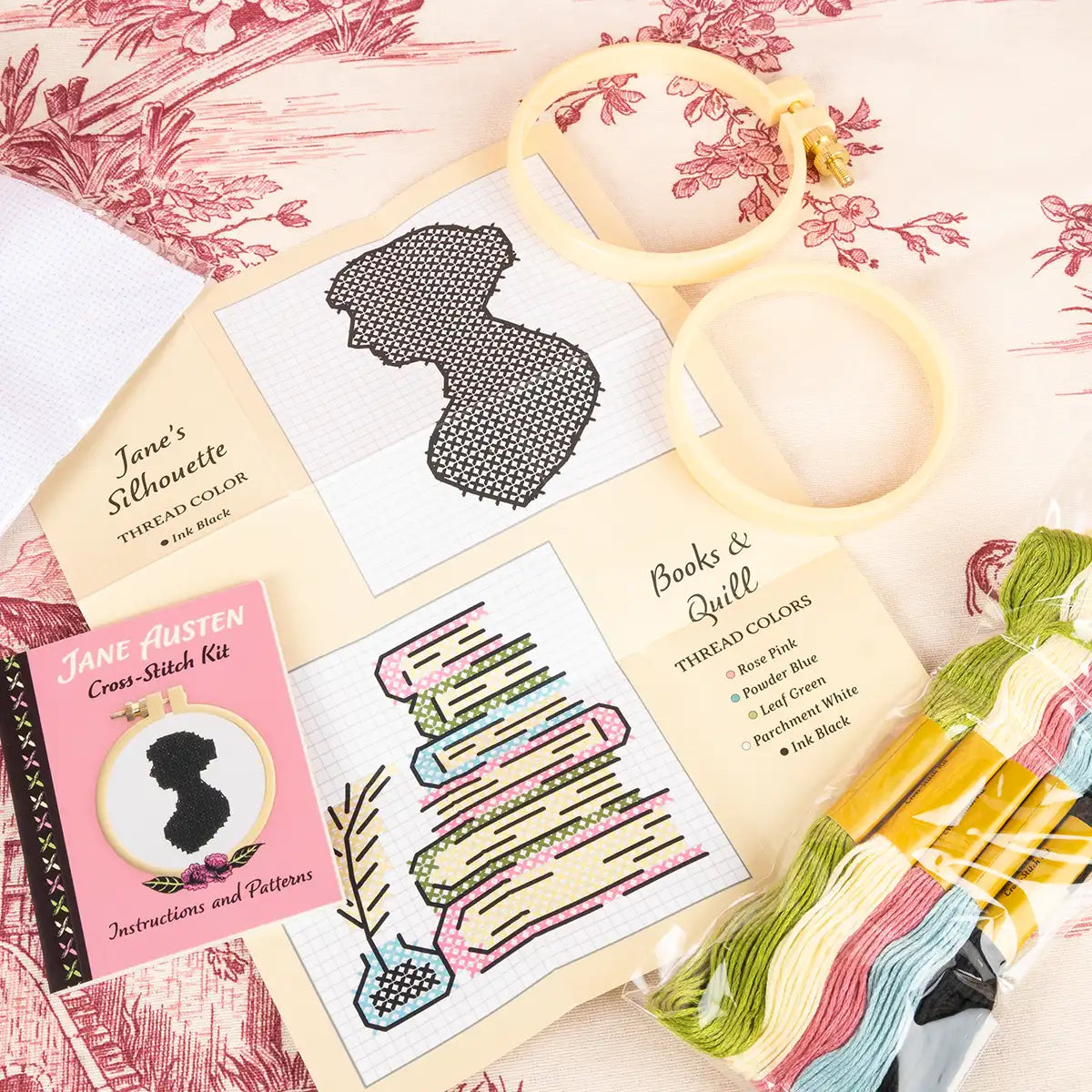 Cross-stitch kit with patterned paper, embroidery hoop, and thread on a floral background