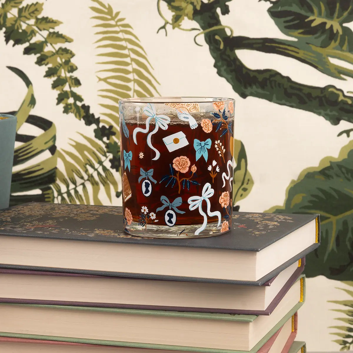 Jane Austen themed glass cup filled with cola on a stack of books against a green forest themed background