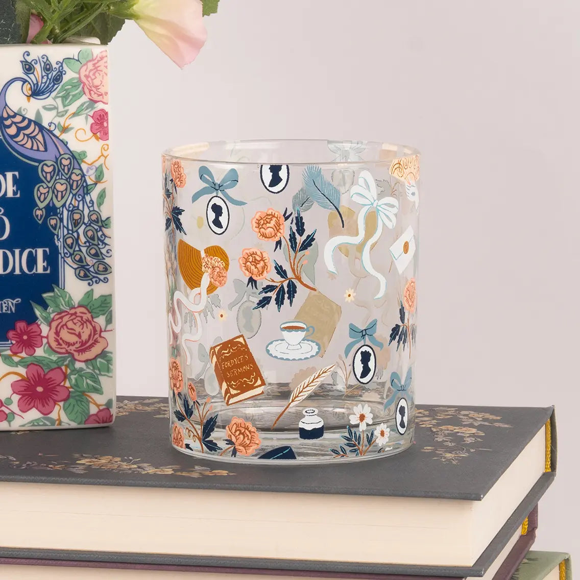 A Jane Austen themed glass tumbler on a stack of books against a white background