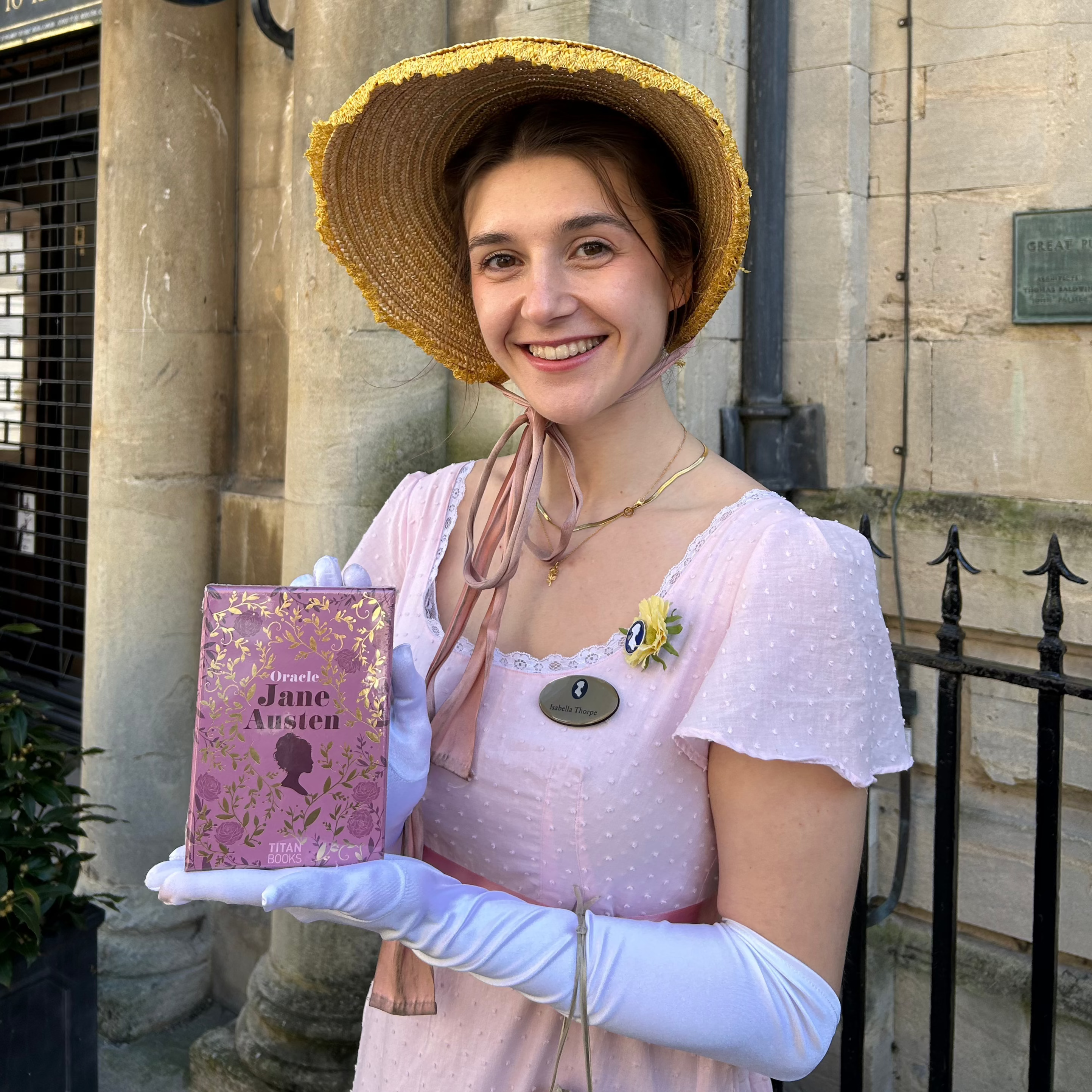 Isabella Thorpe from The Jane Austen Centre holds a pack of Oracle Cards next to a building of Georgian stone.