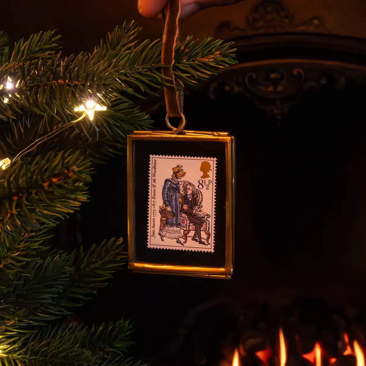 Christmas scene. Someone hanging the decoration on a Christmas tree. In background is a fire and there are fairy lights on the tree.