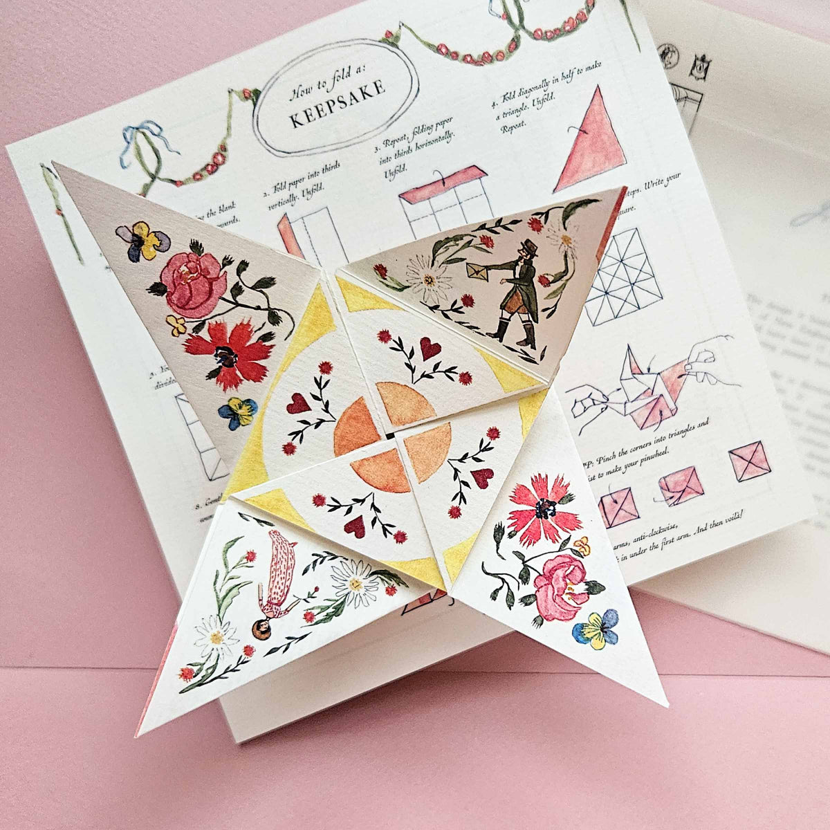 Decorative paper triangles with floral and geometric designs on a pink background