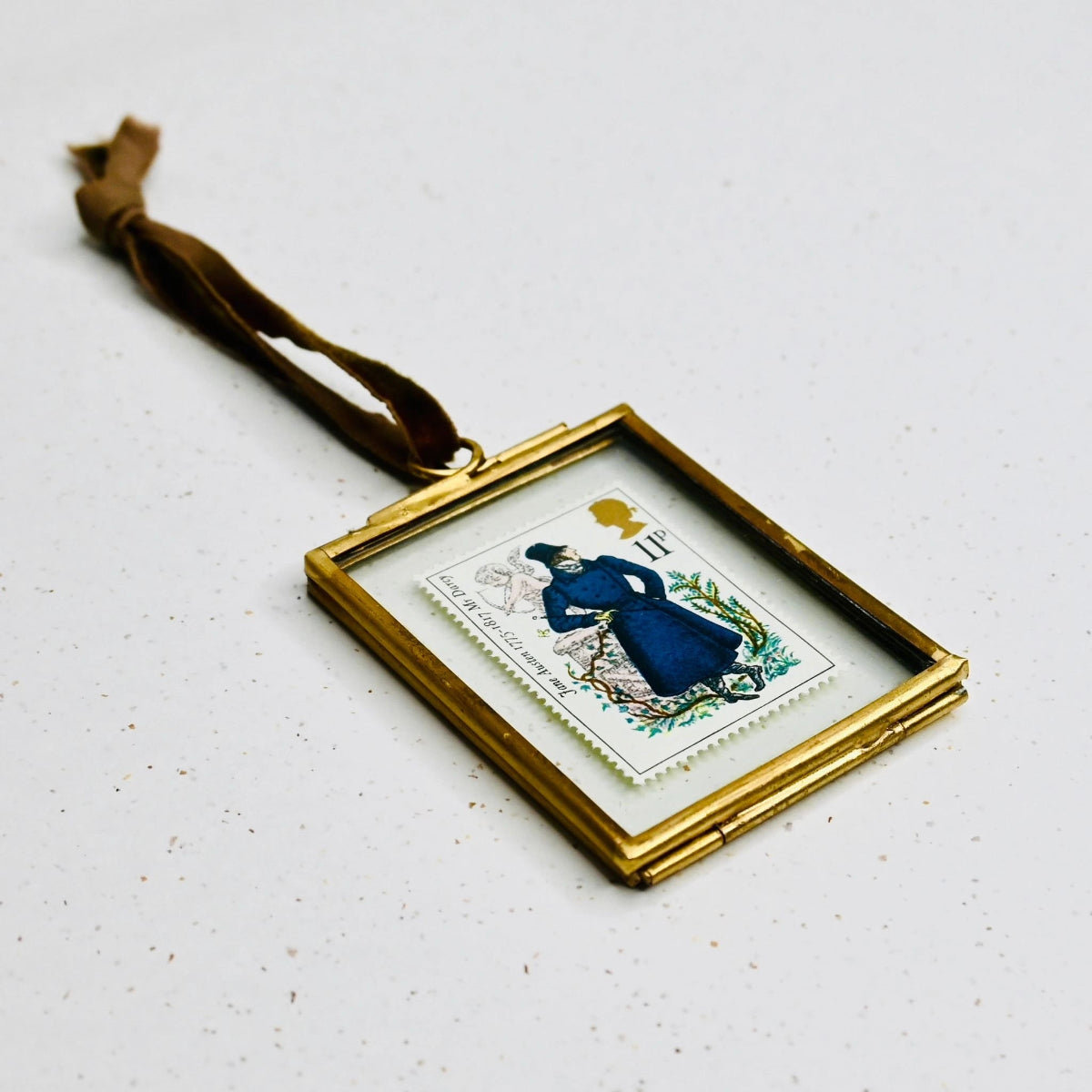 Small framed picture with a brass border laying flat on a white, speckled background.