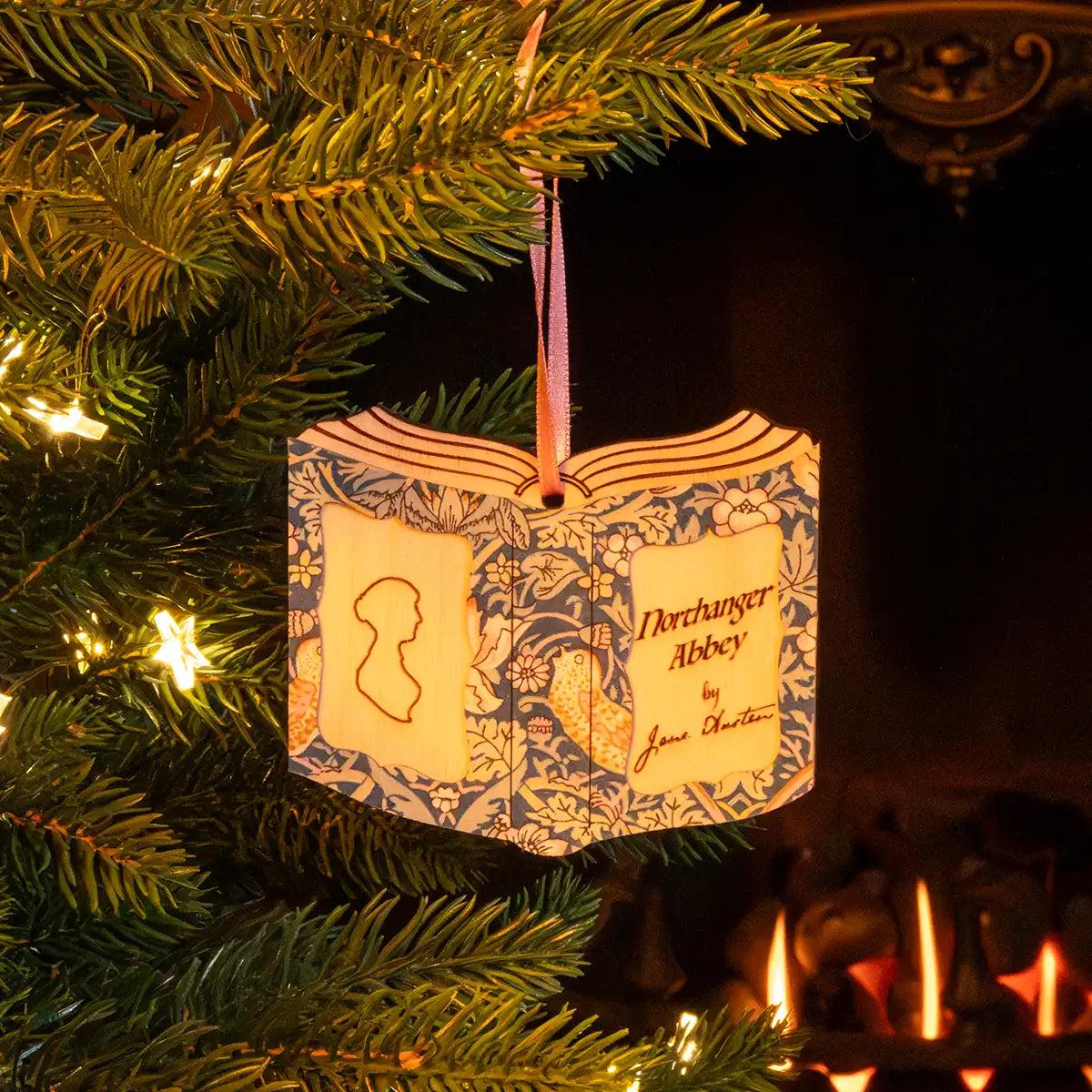 Christmas scene. Someone hanging the decoration on a Christmas tree. In background is a fire and there are fairy lights on the tree.