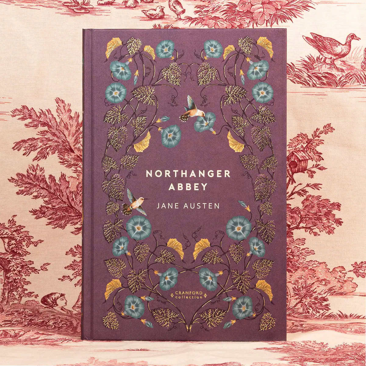 A hardback copy of Northanger Abbey by Jane Austen against a red background patterned with shrubbery and birds