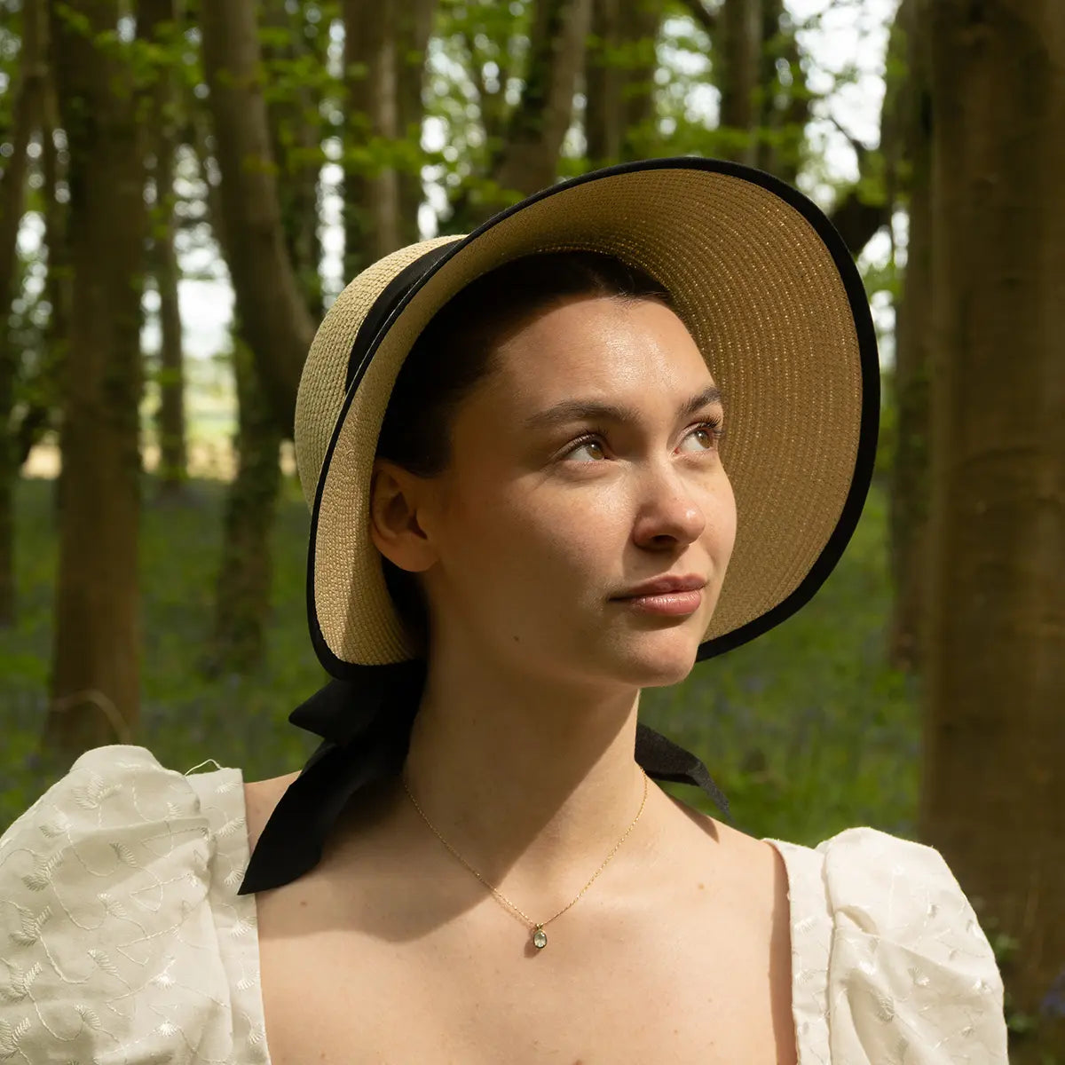 Woman wearing open back regency bonnet in the woods