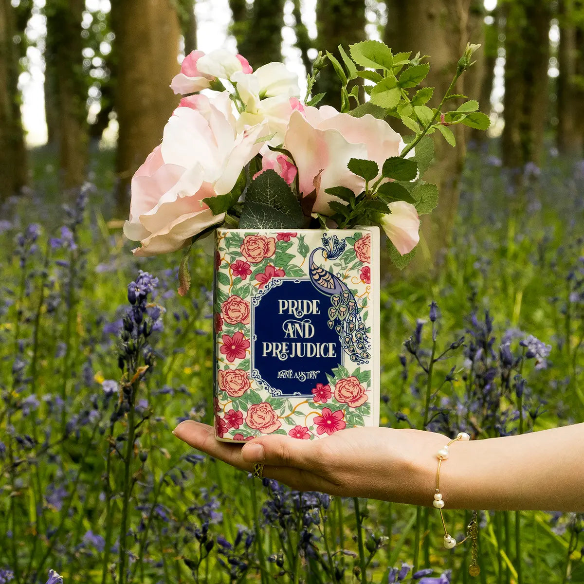 Pride and Prejudice themed ceramic book vase with flowers being held by a hand in a forest