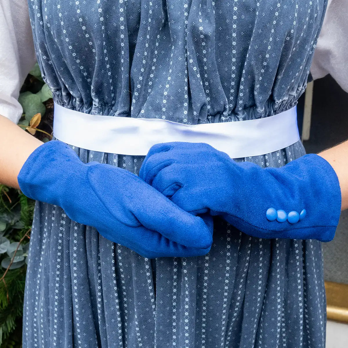 Person wearing blue gloves with a patterned dress and white belt.