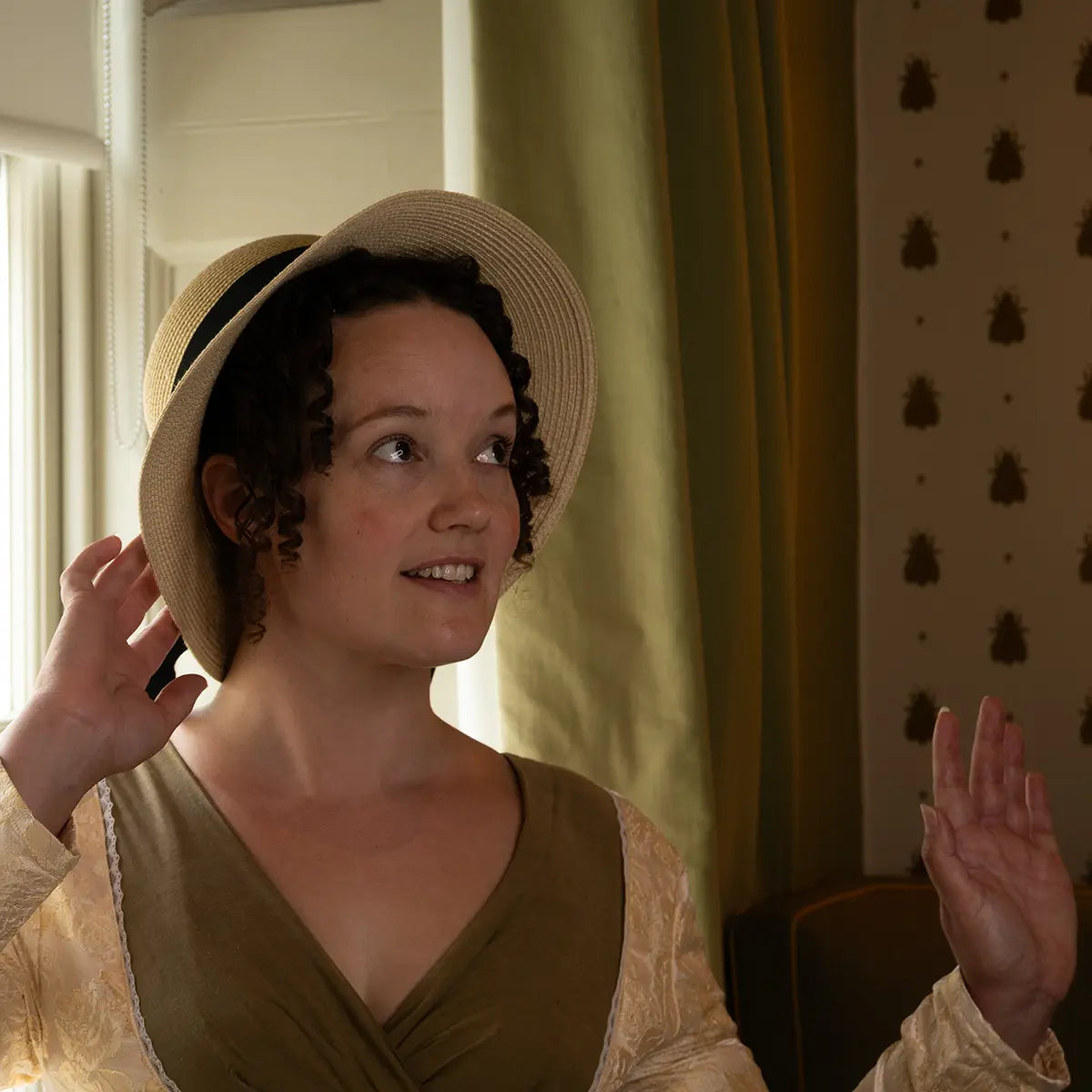 woman wearing a regency bonnet against a background with curtains and insect wallpaper