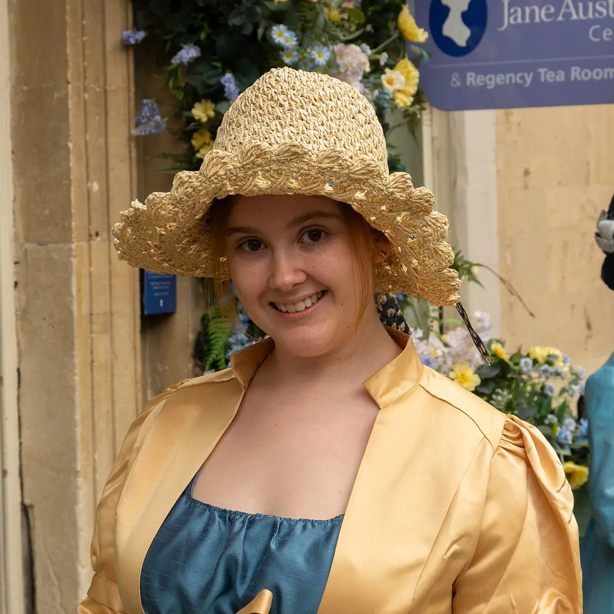 Woman in crochet bonnet and regency clothes stood against will with flowers