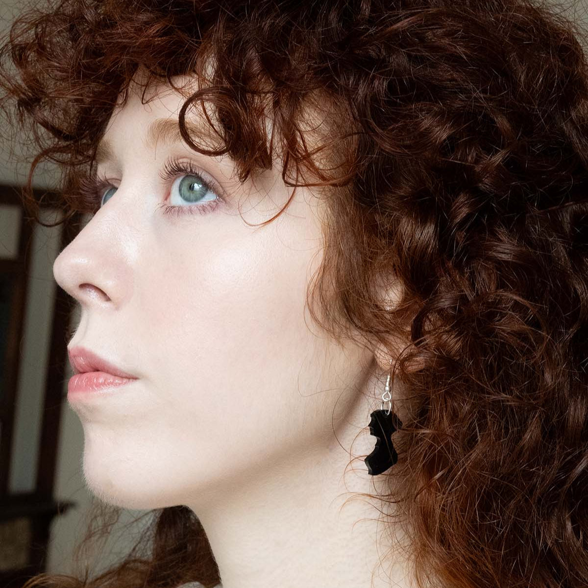 Black acrylic earrings in the shape of Jane Austen's silhouette on a womans ear