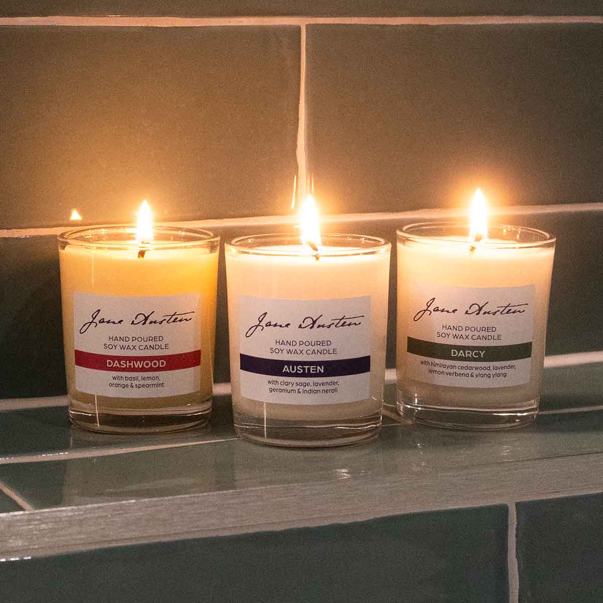 Three candles 'Darcy', 'Austen' and 'Dashwood' lit in warm, glowing bathroom setting.