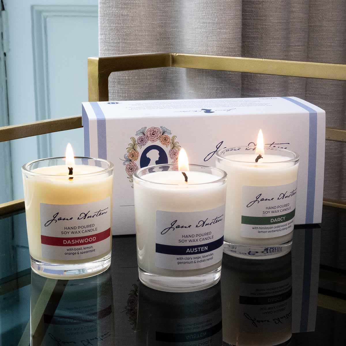 Three candles 'Darcy', 'Austen' and 'Dashwood' lit on a gold edged table.