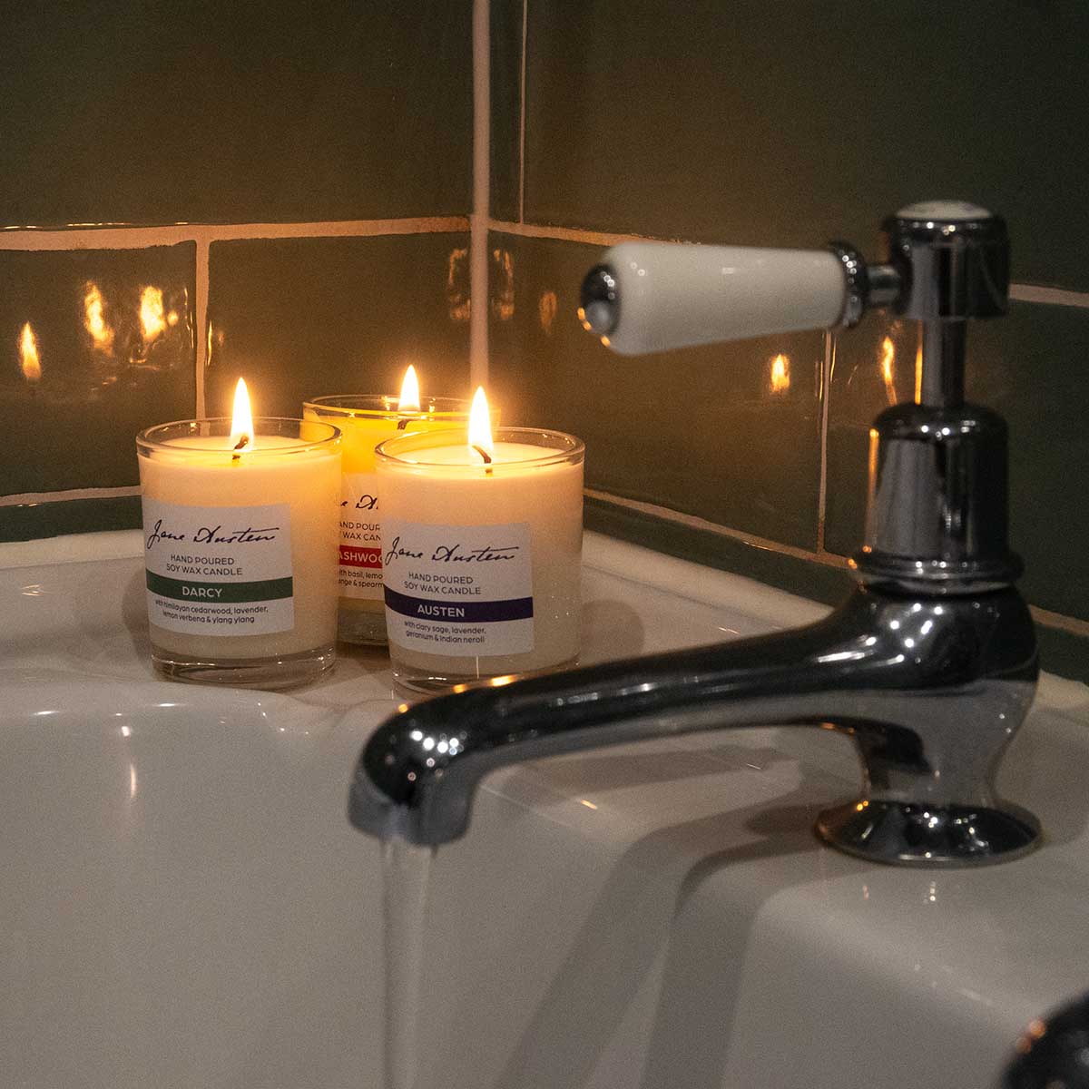 Three candles 'Darcy', 'Austen' and 'Dashwood' lit in warm, glowing bathroom setting.