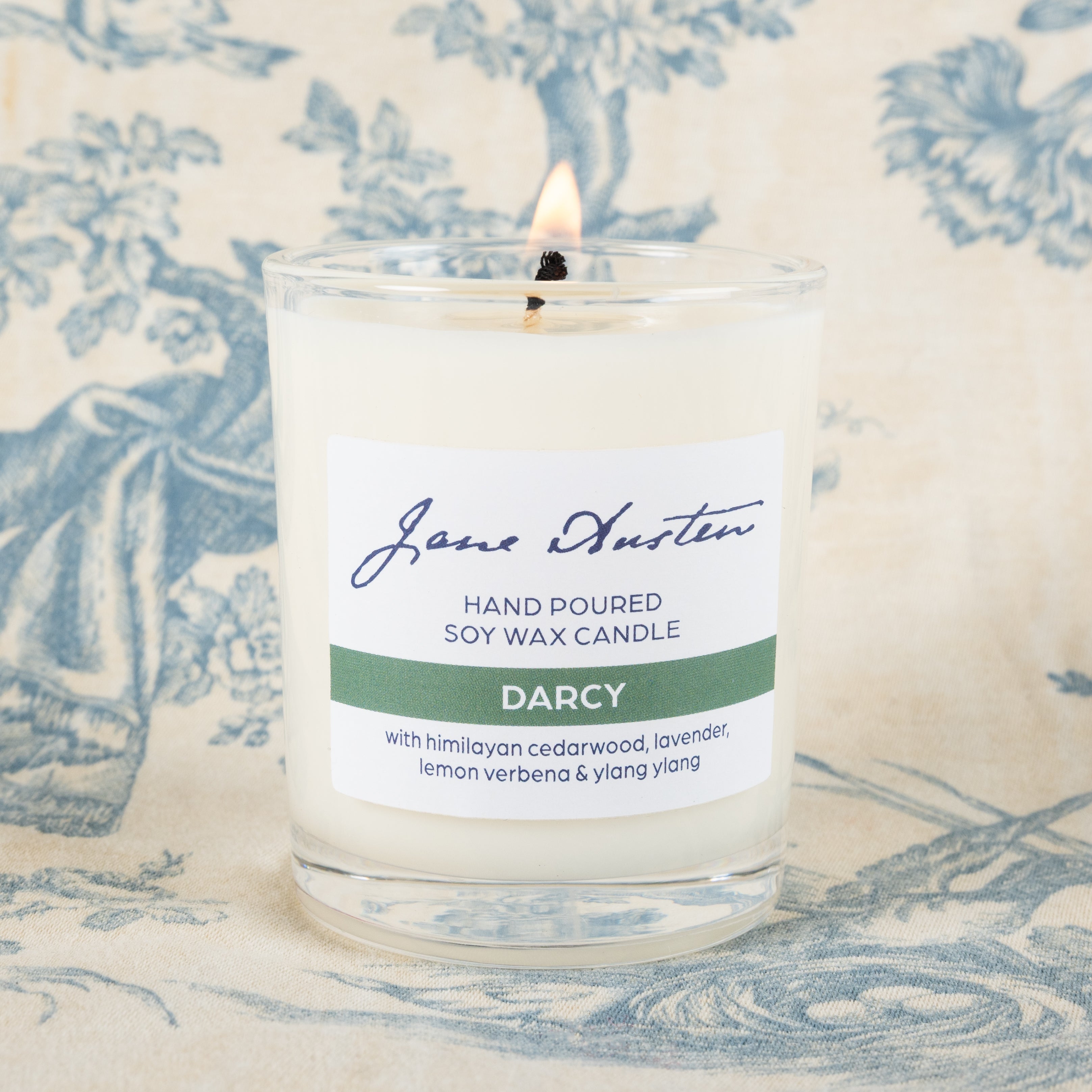 A lit Darcy candle (green label). Hand poured soy wax candle 'Darcy' with Himalayan cedarwood, lavender, lemon verbena & ylang ylang.