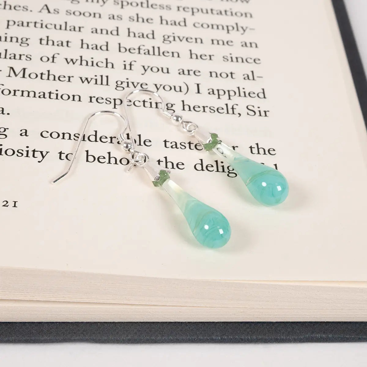 mint coloured glass drop earrinhgs with silver detailing on an open book