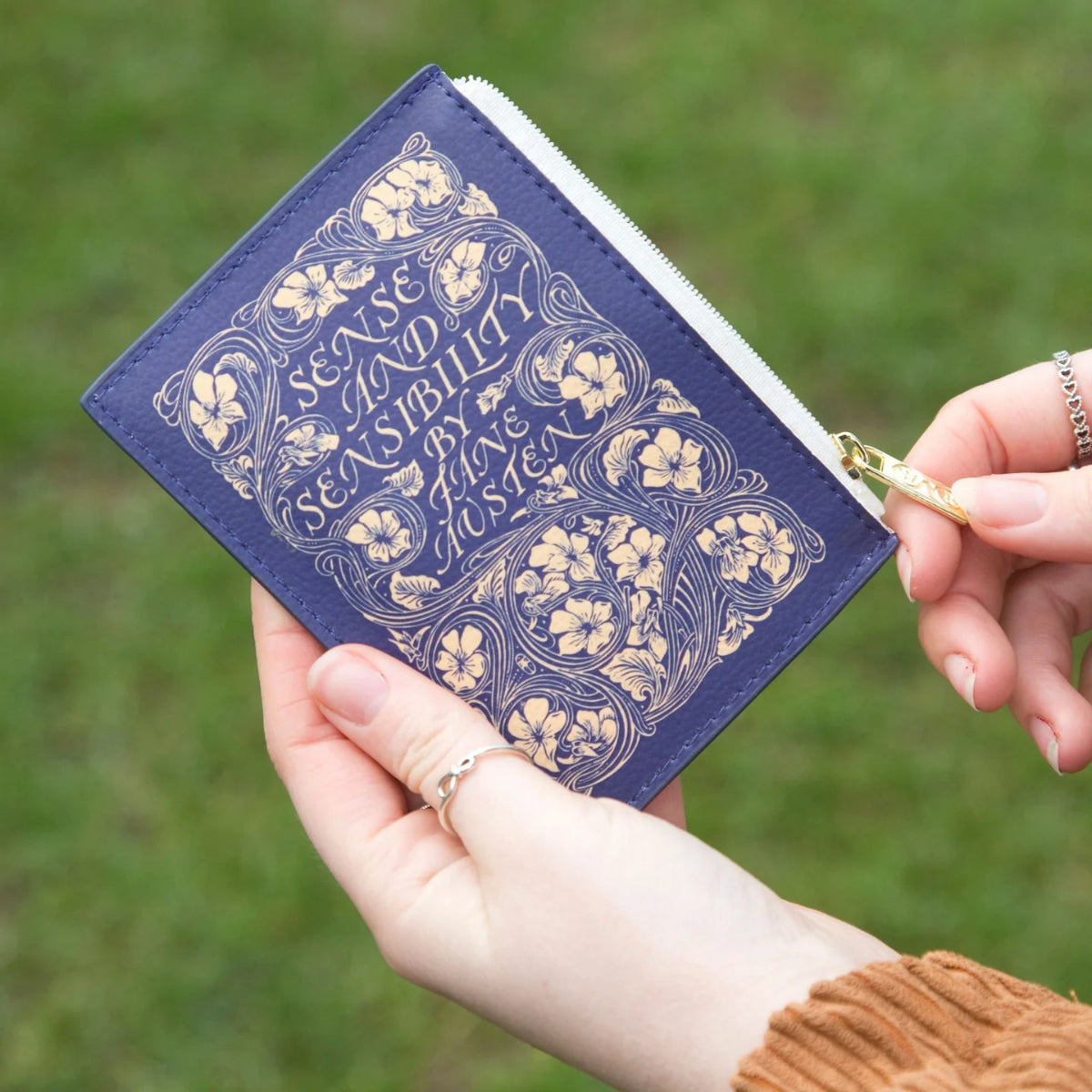 Sense and Sensibility coin purse being held up with grass in the background.
