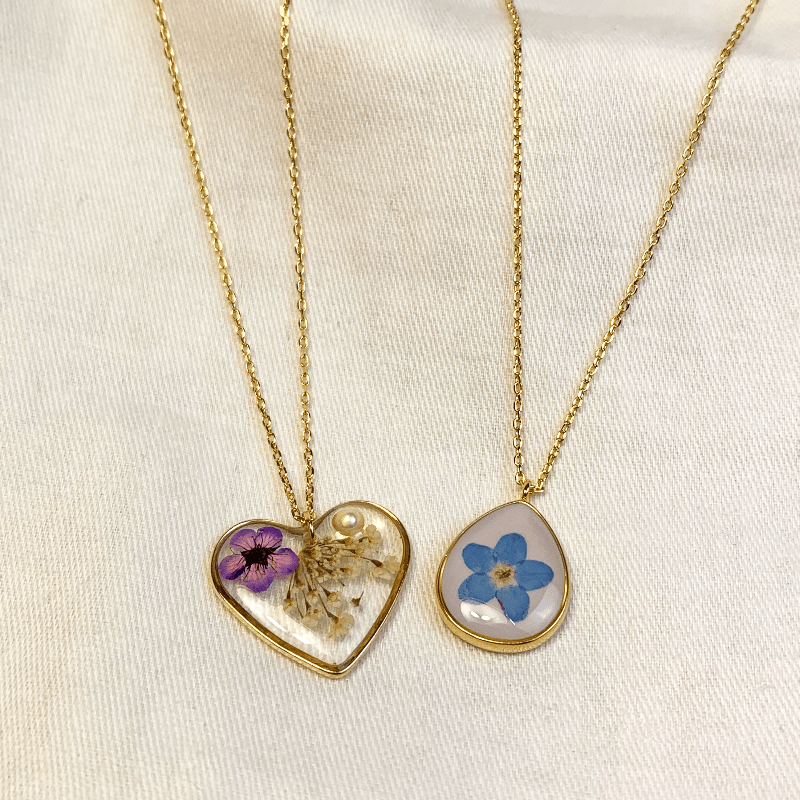 the forget me not necklace is shown here with the heart of longbourn necklace. The necklace has a heart shaped pendent with flowers and a pearl inside the pendent in resin Jane Austen Jewellery