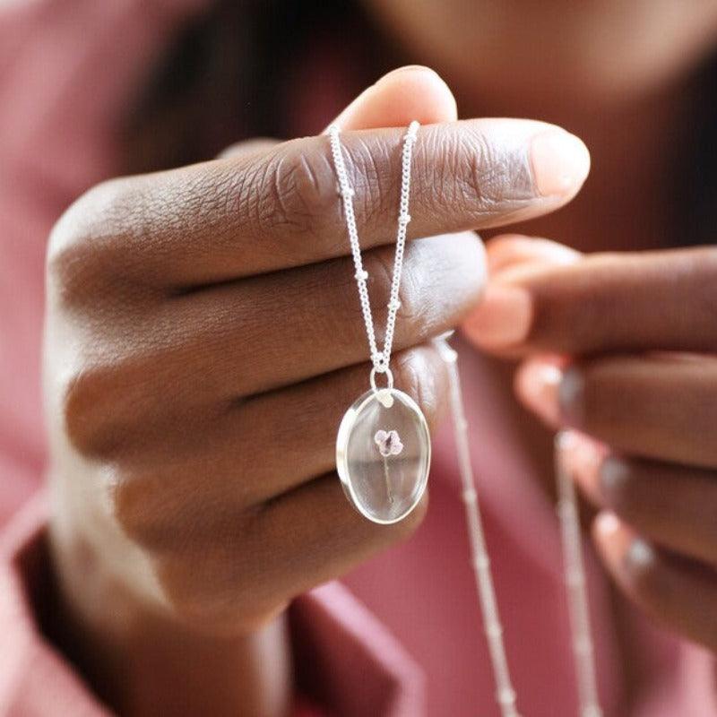 The november necklace is held out to show the delicate flower incased in resin