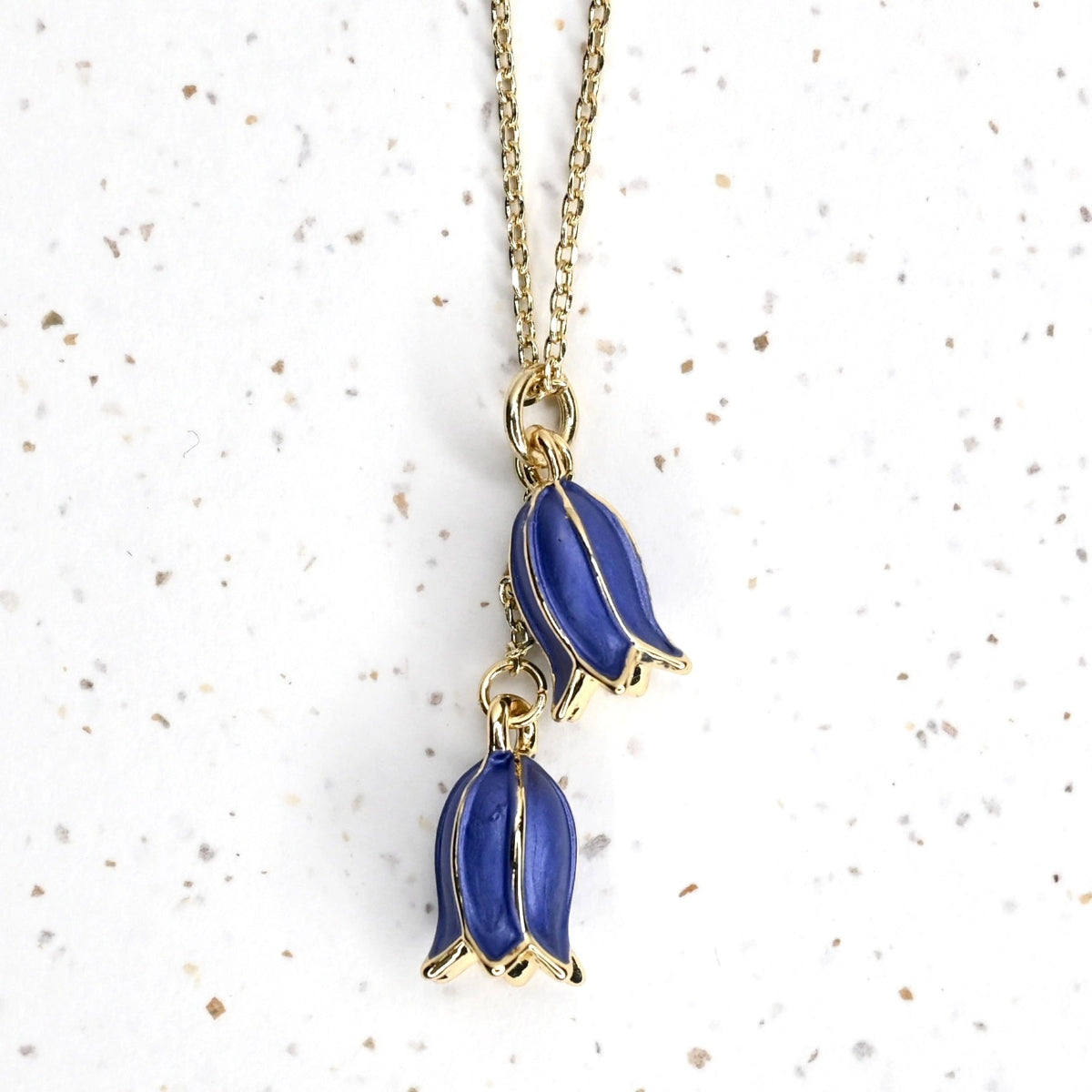 Closeup of 2 bluebells hanging from a gold necklace