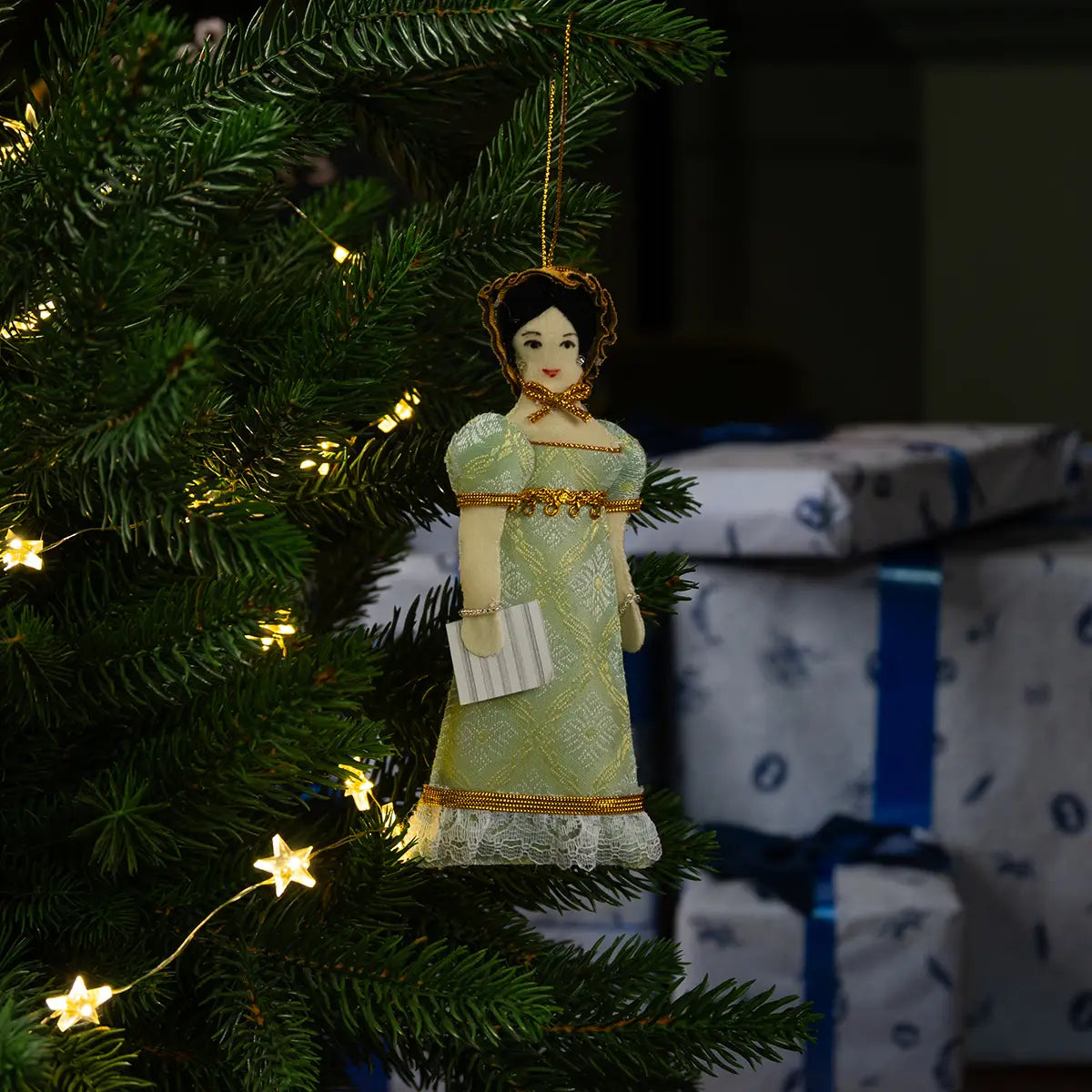 Decorative Christmas ornament of Anne Elliot, hanging on a tree with a fireplace in the background.