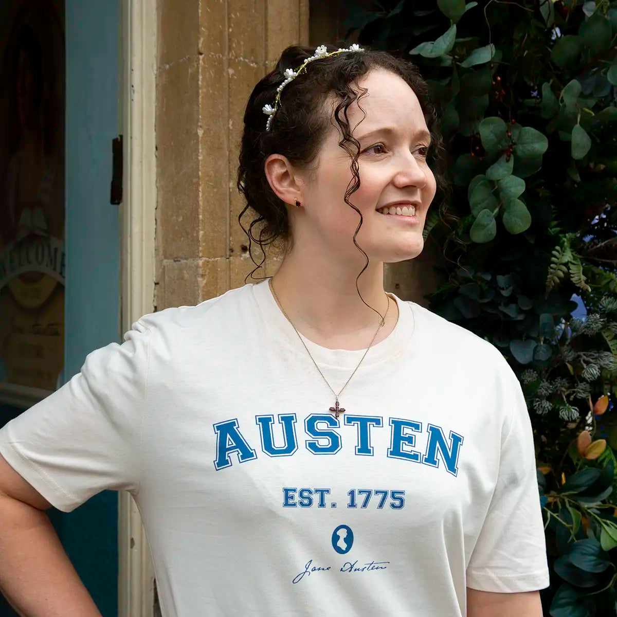 Woman in tiara outside wearing a cream shirt with 'AUSTEN EST. 1775' and Jane Austen silhouette printed in blue. 