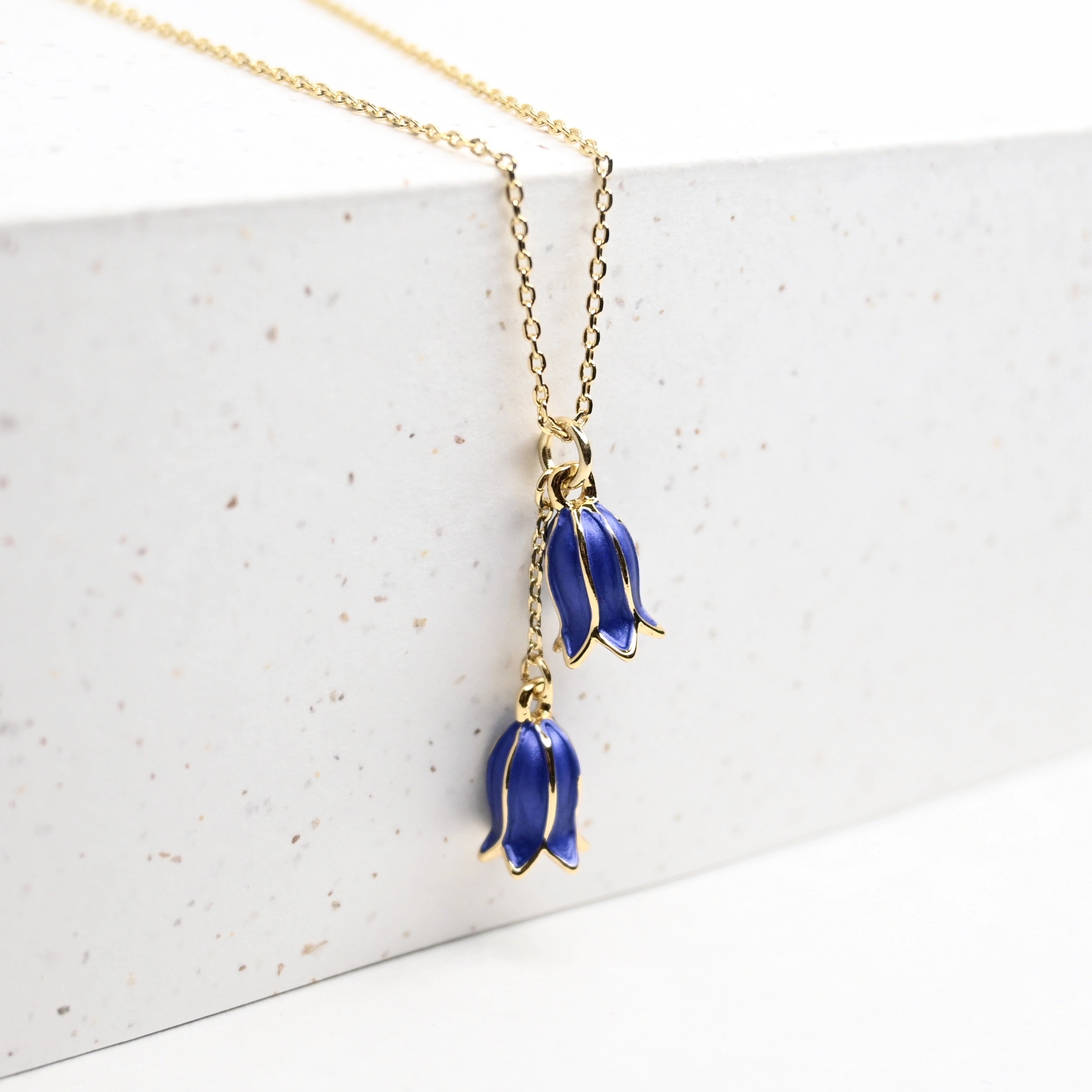 Closeup of a gold necklace with 2 bluebells hanging over an edge