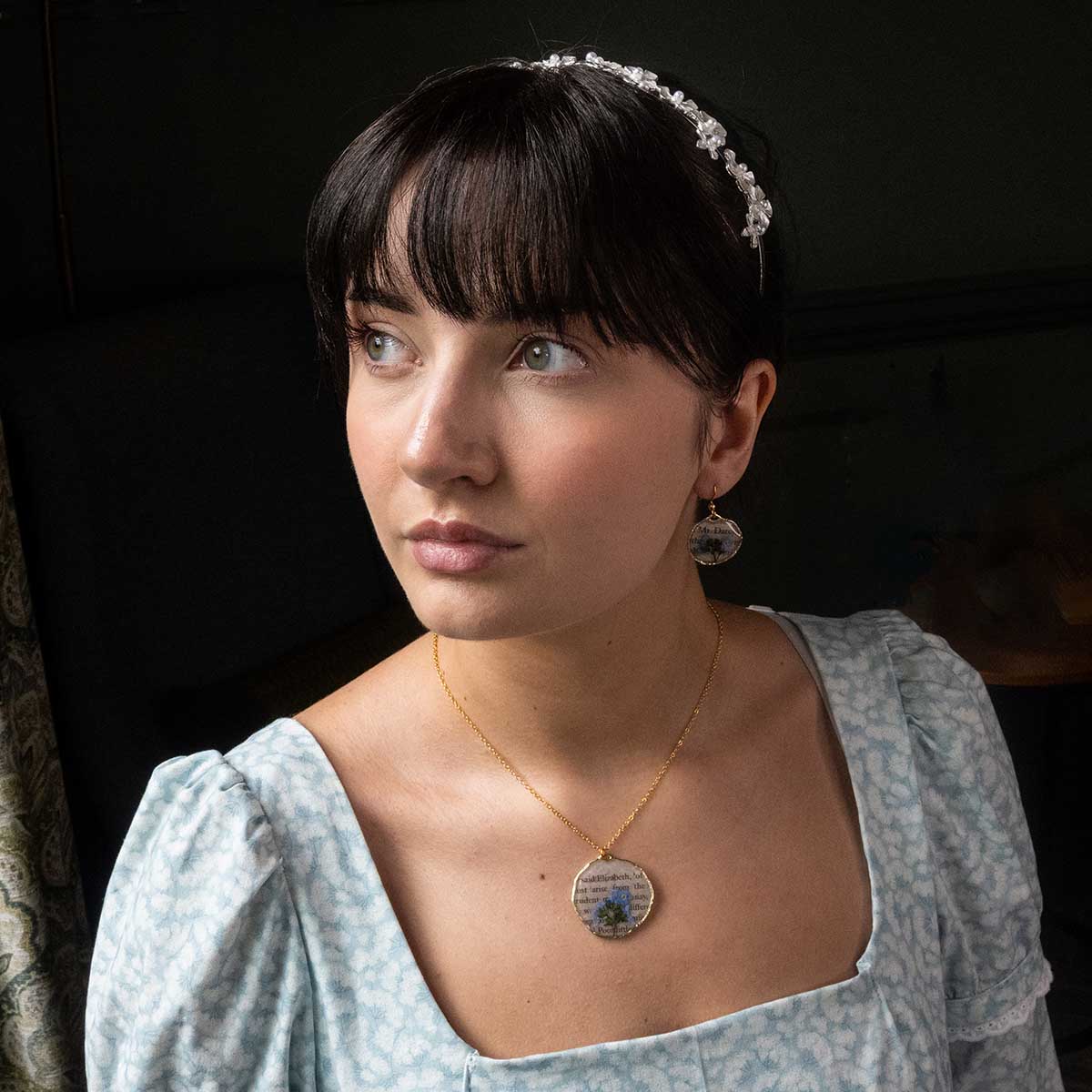 Catherine Morland modelling Book Page Earrings and Necklace, gazing out of a window.