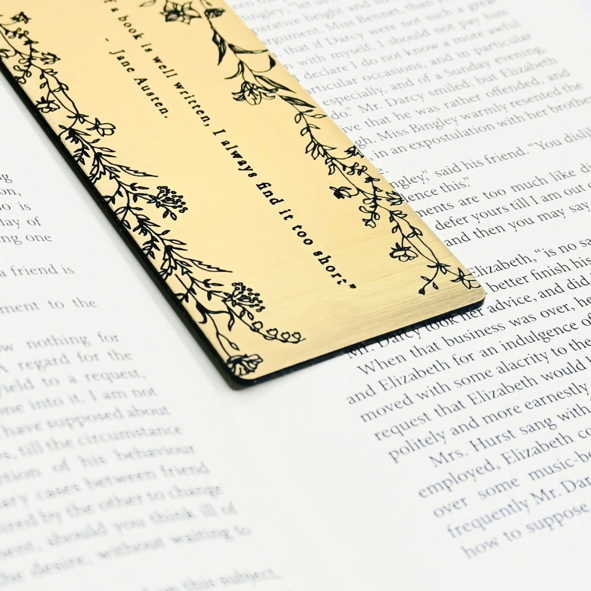 Close up of a bookmark  with brushed gold acrylic featuring an engraved quote 'but for my own part, if a book is well written, I always find it too short' - Jane Austen.
