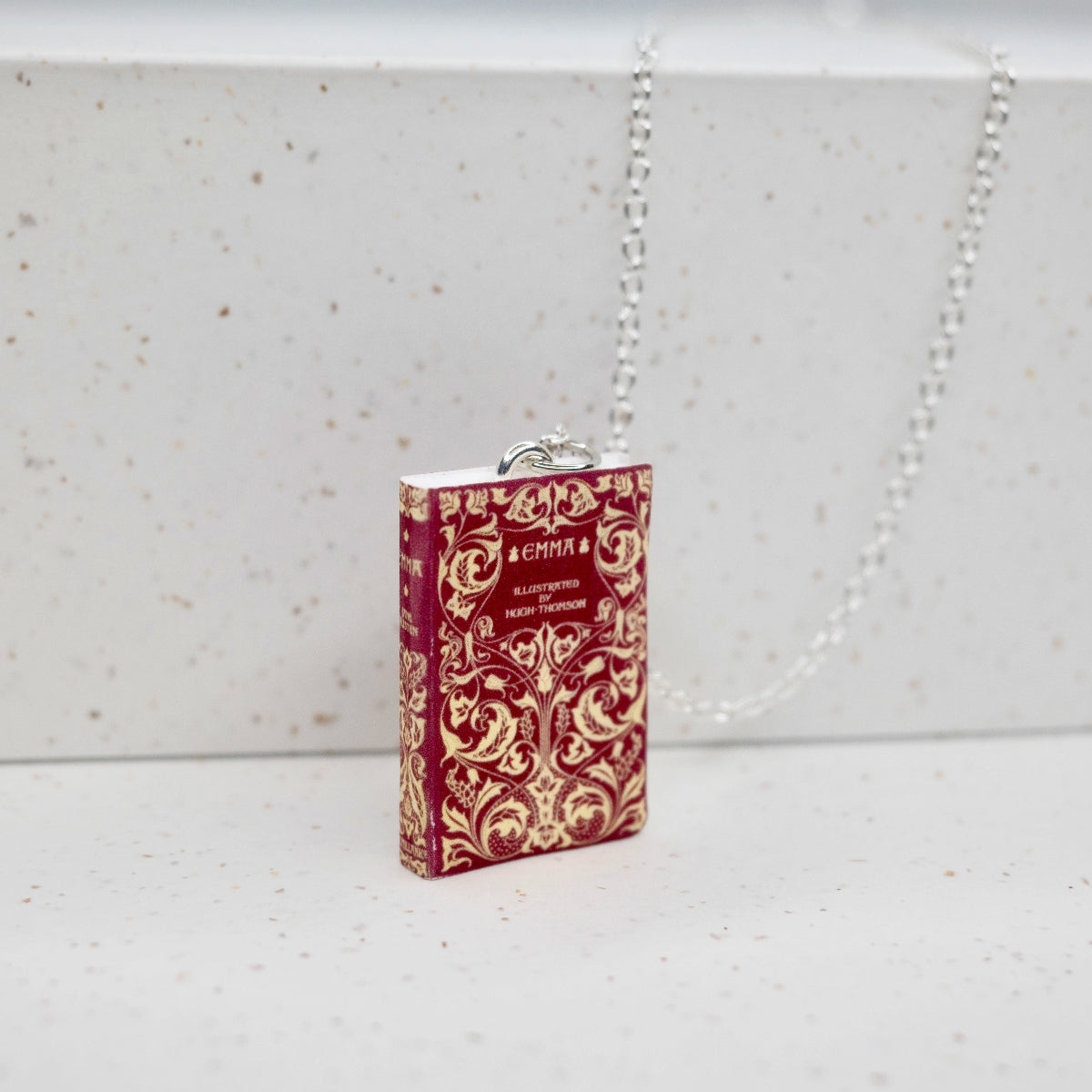 Emma book necklace in front of a speckled, white backdrop.