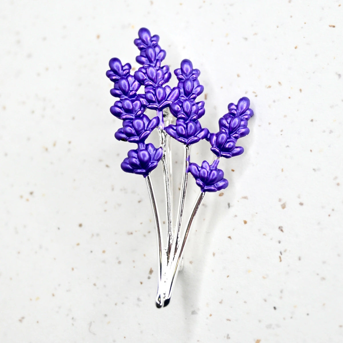 A silver-colored brooch featuring vibrant purple lavender flowers and a silver-colored pin backing.