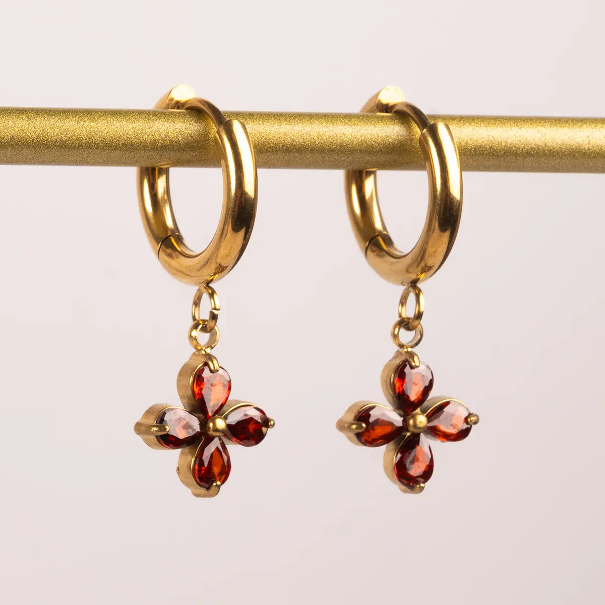 Elizabeth Bennet huggie red garnet earrings hanging from a gold bar against a white background
