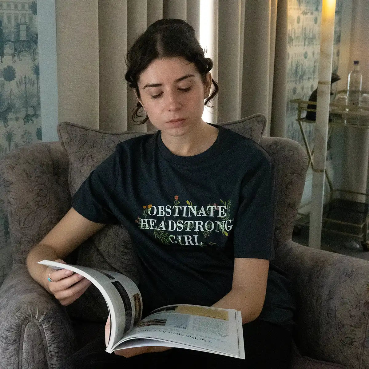 Model reading a magazine while wearing a black t-shirt in an armchair.