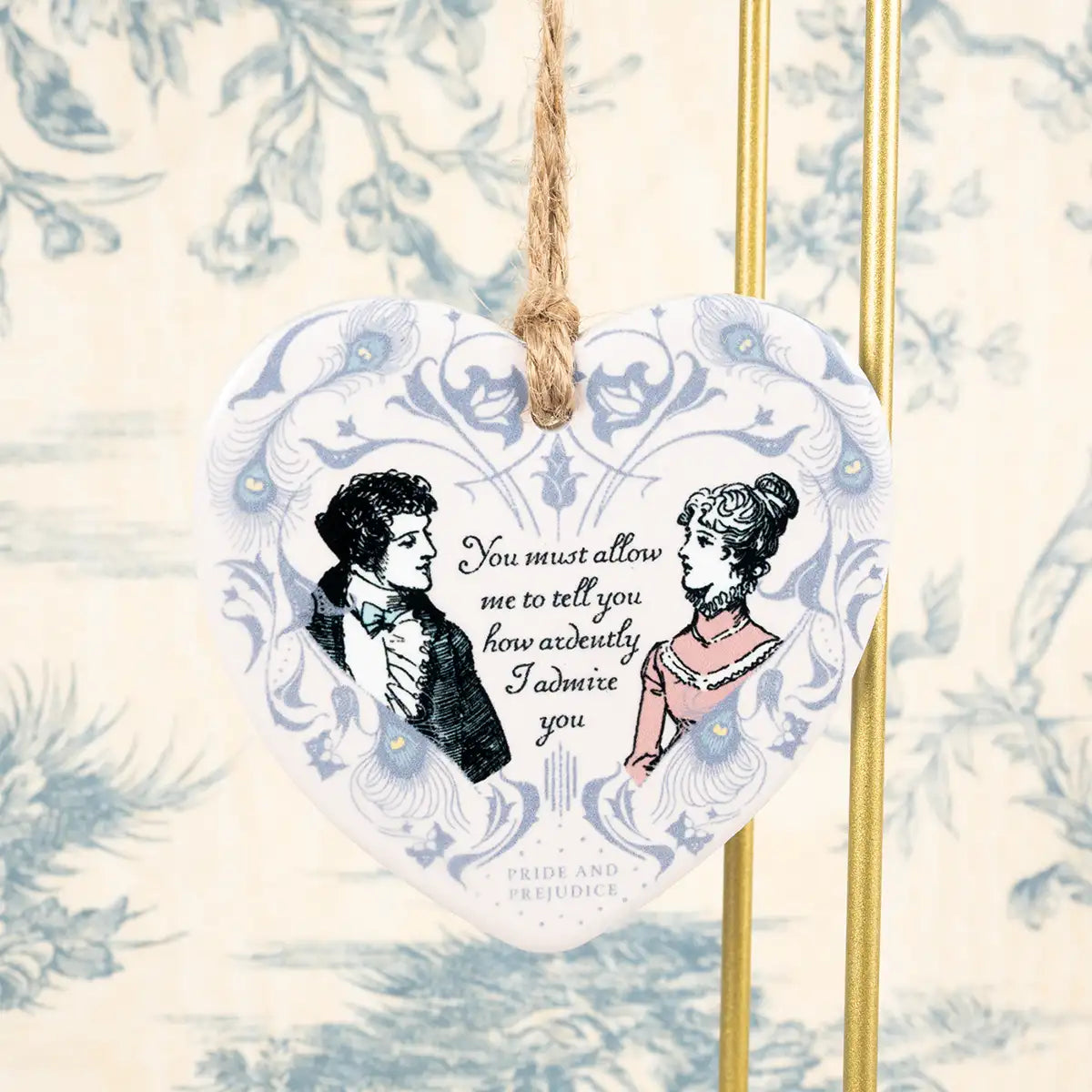 Heart-shaped ceramic tag with vintage-style illustration of a couple and text, hanging against a decorative background.
