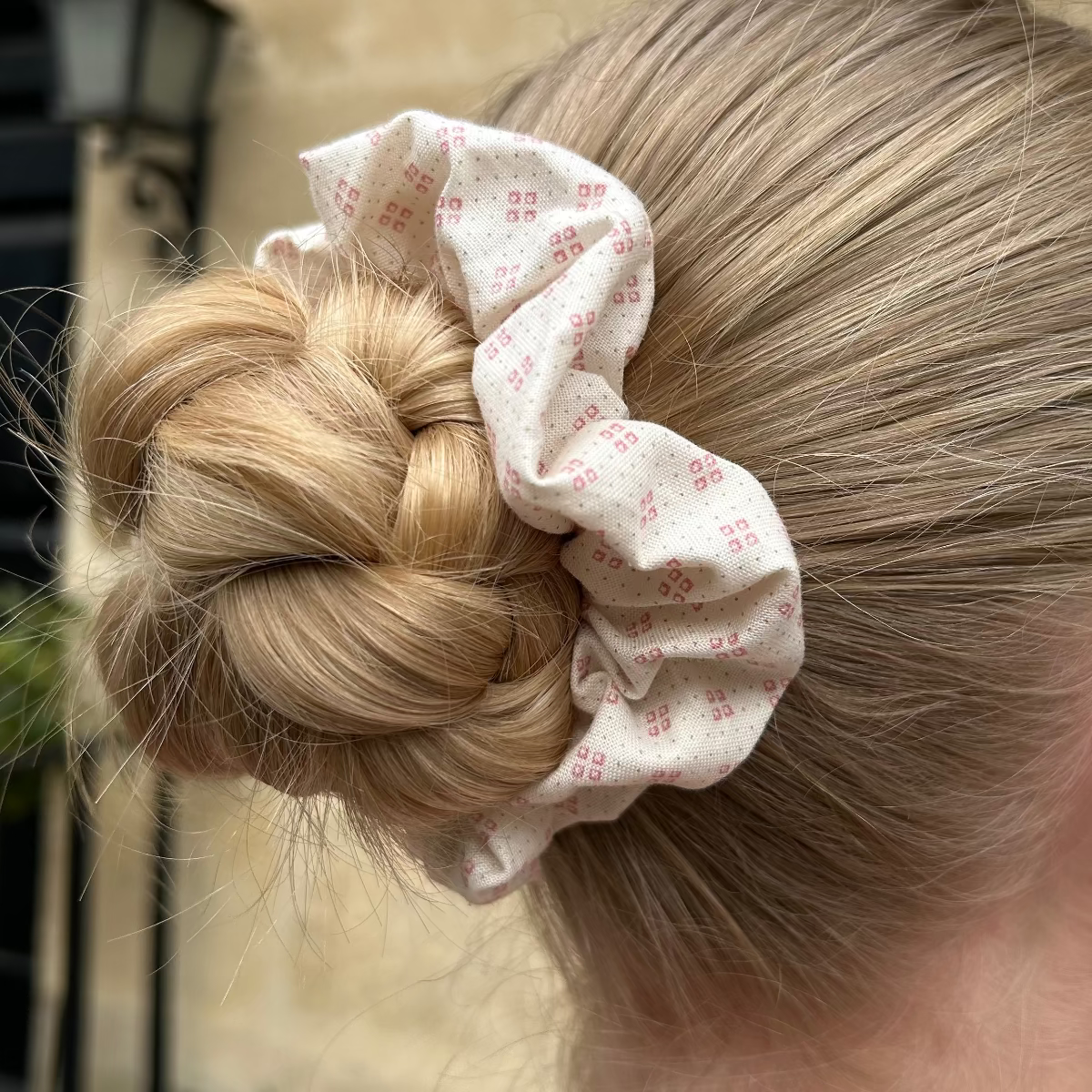 Pink patterned scrunchie shown on hair in a bun. 