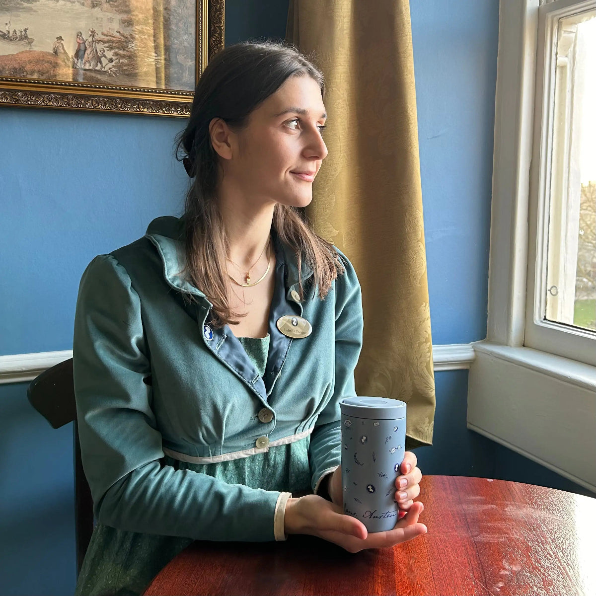 Woman holding a mug in a room with blue walls and a window.