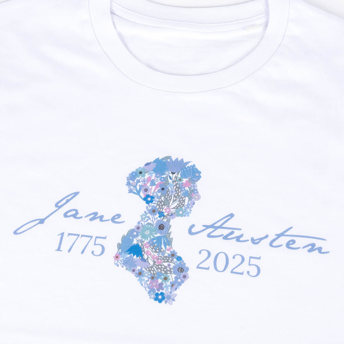 Close-up. Jane Austen 250th Anniversary T-Shirt in White. Silhouette of Jane is filled with flowers in cool tones and text 'Jane Austen 1775-2025' is in a cool tone of blue.