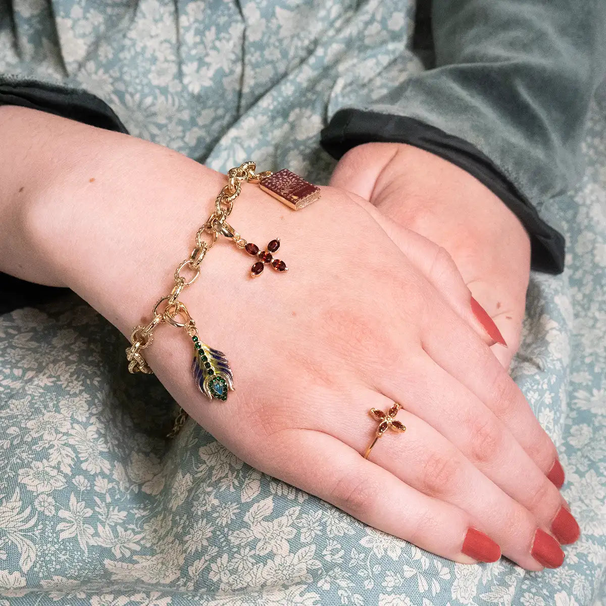 Close-up of a hand wearing a gold bracelet with charms on a floral fabric background
