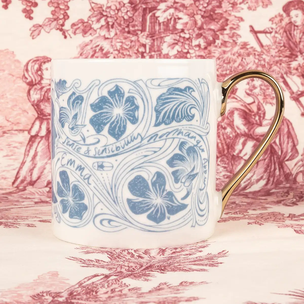 Side views. Cream mug decorated in swirling blue flower illustrations and the names of Jane Austen's novels. Gold handle.