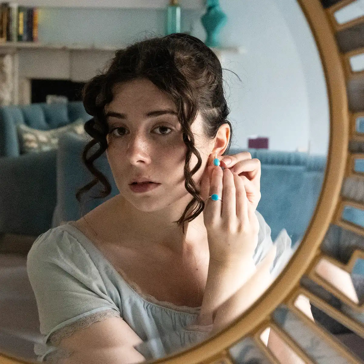 Woman adjusting earrings in front of a large round mirror.
