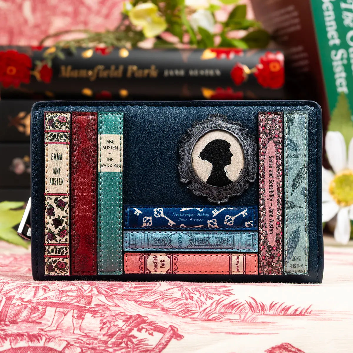 Lifestyle shot of blue flap over jane austen purse with books and flowers in the background
